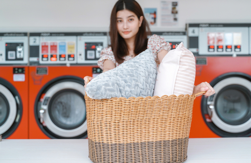 Young,Millennial,Asian,Woman,Showing,Basket,Of,Clothes,And,Pillow