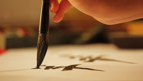 Close,Up,On,Hand,Holding,Brush,While,Writing,Calligraphy