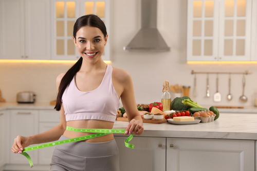 Happy,Woman,Measuring,Waist,With,Tape,In,Kitchen.,Keto,Diet